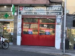 Fachada de "Carrocerías López" con puertas rojas, al lado de una farmacia y una motocicleta.