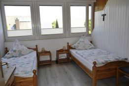 Zwei Betten in einem hellen Zimmer mit drei Fenstern und Holzverkleidung an der Wand.