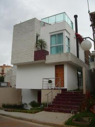 Casa moderna de dois andares com fachada branca e detalhes em vidro e pedra.