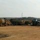 Tractor with trailers on a dirt field under a cloudy sky.