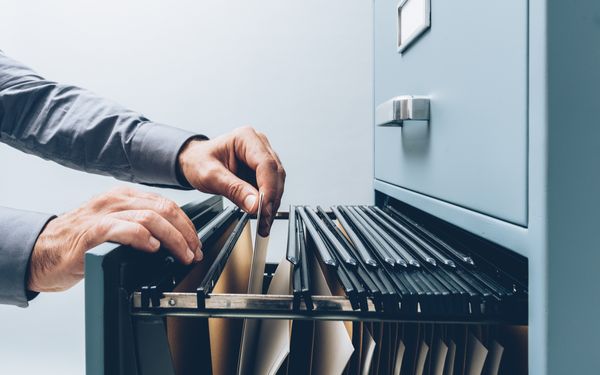 Person zieht Personalakte aus einem Aktenschrank.
