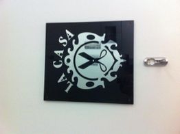 Schwarzes Schild mit Schere-Logo und dem Schriftzug "La Casa" in weißen Buchstaben an der Wand.