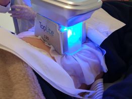 Person unterzieht sich einer Behandlung mit einem blauen Lichtgerät namens "Toplite 130".