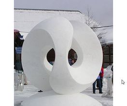Eine große, abstrakte Schneeskulptur mit ineinandergreifenden Ringen auf einem schneebedeckten Platz.