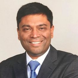 A person in a suit smiling against a plain background.