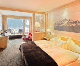 Gemütliches Hotelzimmer mit Doppelbett, Bergbild an der Wand und Fensterblick auf verschneite Berge.