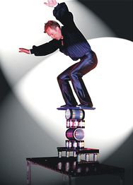 Ein Artist balanciert auf gestapelten Rollen auf einer Bühne im Scheinwerferlicht.