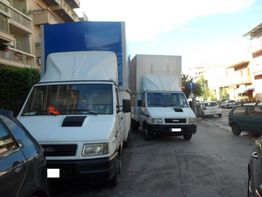 Due furgoni bianchi parcheggiati di lato su una strada cittadina, edifici sullo sfondo.