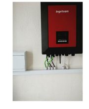 Inversor rojo de pared con cables verdes y negros conectados, caja blanca al lado.