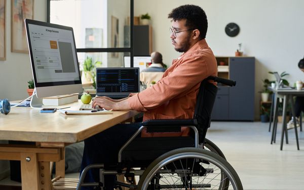 Mann im Rollstuhl arbeitet an einem Computerarbeitsplatz mit einer Anwendung zur KI-Bildgenerierung.