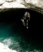 Persona buceando en cenote, colgada sobre el agua azul, rodeada de paredes rocosas.