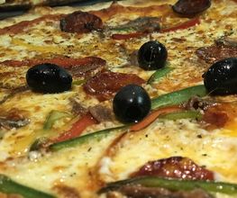Pizza mit schwarzen Oliven, Paprika, Wurst und geschmolzenem Käse.