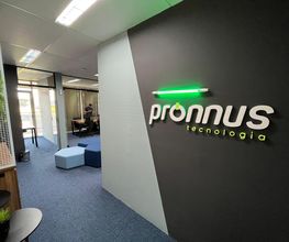 Corredor de escritório com parede preta e logo "pronnus tecnologia", piso azul e móveis de trabalho.