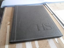 Carpeta negra con las letras "HS" estampadas sobre una mesa.