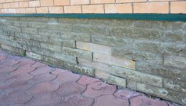 Brick wall with green trim above a red patterned sidewalk.