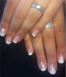 Nahaufnahme von Händen mit French Maniküre und silbernen Ringen auf schwarzem Hintergrund.