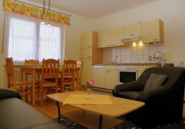 Wohnzimmer mit schwarzem Sofa, Esstisch und Küchenzeile mit Herd, Schränken und Mikrowelle.