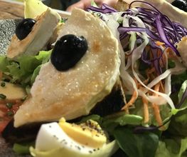 Salat mit geröstetem Brot, Käse, schwarzen Oliven, Eiern und buntem Gemüse auf einem Teller.