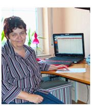 Person am Schreibtisch mit Laptop, trägt gestreiftes Hemd. Fenster, Pflanzen im Hintergrund.