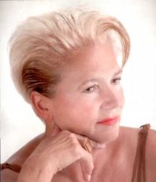 Frau mit blondem, kurzen Haar schaut nach rechts, trägt einen Ring und hat die Hand am Kinn.