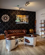 Gemütliches Wohnzimmer mit Ledersofa, Wanduhr, Wandbild, und Bücherregal auf Holzboden.