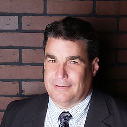 Man in a suit and tie standing against a brick wall.