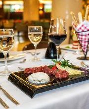 Mesa elegante con copas de vino y plato de embutidos sobre mantel blanco en restaurante iluminado.