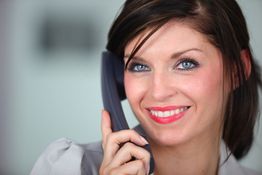 Frau telefoniert lächelnd mit grauem Telefonhörer, Nahaufnahme ihres Gesichts.