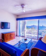 Sala de estar luminosa con vistas al mar, sofá azul, TV y mesa de centro, salida a balcón.