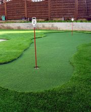 Minigolfplatz im Garten mit grünem Kunstrasen und zwei rot-weißen Fahnen.