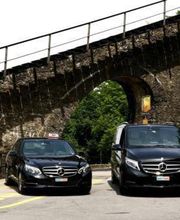 Zwei schwarze Mercedes-Taxis stehen unter einem steinernen Viadukt auf einer Straße.