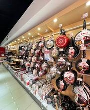 Estante de tienda con diversas sartenes colgadas y productos de cocina exhibidos.