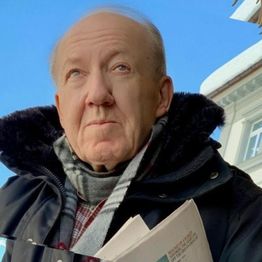 Ein Mann im Wintermantel und Schal blickt nachdenklich in die Ferne, blaues Himmel im Hintergrund.