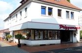 Eckgebäude mit Ladenfront, roten Buchstaben, großen Fenstern und Pflanzen neben dem Eingang.