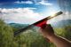 Hand hält Fensterabzieher, reinigt Scheibe mit Blick auf hügelige Landschaft und blauen Himmel.