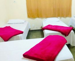 Quarto com camas cobertas com lençóis brancos e cobertores vermelhos, cortina amarela ao fundo.