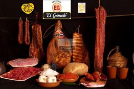 Variedad de embutidos y quesos "El Gemelo" sobre mesa con fondo oscuro.