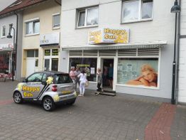 Ein kleines Auto vor einem Laden namens "Happy Sun". Menschen stehen vor dem Eingang.