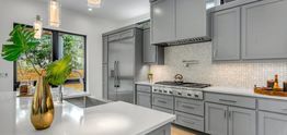 Modern kitchen with grey cabinets, stainless steel appliances, and white countertops.