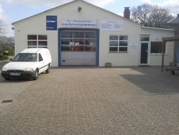 Weiße Werkstatt mit Lieferwagen davor, blauer Torbogen, Schilder "Auto Service Ganderkesee".