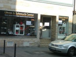 Schaufenster eines Uhren- und Schmuckgeschäfts mit 30% Rabatt, silbernes Auto im Vordergrund.