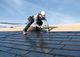 Worker installing solar panels on a rooftop under a blue sky.