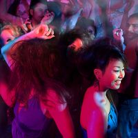A lively group of people dancing energetically in a colorful, dimly lit nightclub.