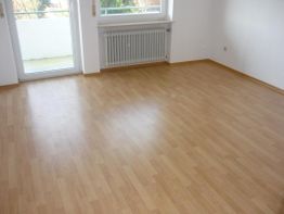 Leerer Raum mit Holzfußboden, Heizkörper und Fenster zur Terrasse.