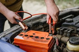 Person attaching jumper cables to a car battery.