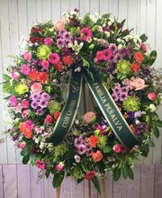 Corona floral colorida con cinta verde dedicada a "FAMILIA PEÑALVA".