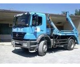 Blauer Lastwagen mit Kranarm vor einem Gebäude geparkt.