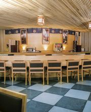 Interior de un restaurante con barra de sushi, sillas de madera y techo de listones.