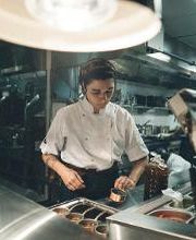 Chef preparando comida em cozinha industrial bem iluminada.