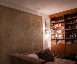 Wohnzimmer mit braunem Sofa, Bücherregal, Lampe und einem Hund auf dem Boden.